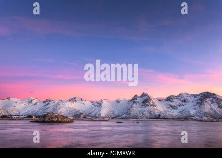Belle montagne coperte di neve e cielo colorato riflessa nell'acqua di notte. Paesaggio invernale con mare, rocce innevate, sky, Nuvole rosa, riflessione a Foto Stock