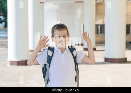 Il ragazzo è un primo-grader in una t-shirt bianca con un zaino grigio. diverse emozioni. torna a scuola Foto Stock