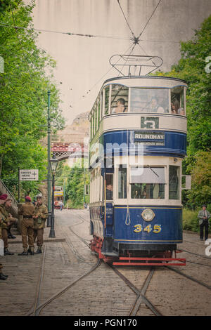 Vintage street scene (effetto invecchiato) mostrante conservati doppio ponte di Leeds il tram 345, viaggiando su strada di ciottoli a Crich Tramway Museum a 1940s'evento. Foto Stock