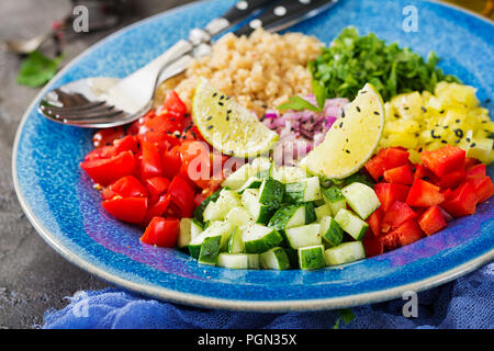 Con insalata di quinoa, rucola, peperoni, pomodori e cetrioli in ciotola su uno sfondo scuro. Cibo sano, dieta disintossicante e concetto vegetariano. Buddh Foto Stock