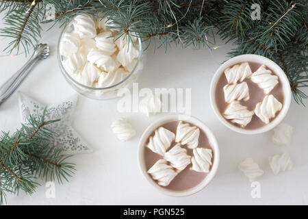 Il cacao con marshmelow in bianco tazze e marshmallows in un vasetto di vetro su un tavolo bianco con rami di abete rosso, una ghirlanda di fiori e una stella bianca. Messa a fuoco selettiva Foto Stock