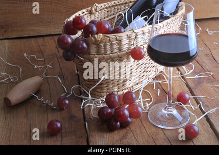 Uve su un cestello per servire il vino con una bottiglia e un wineglass su legno sfondo rustico Foto Stock