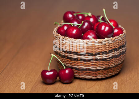 Red ciliegie mature in un cesto su una tavola di legno Foto Stock