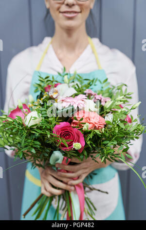 Vista del raccolto di closeup giovane fioraio in uniforme di lavoro tenendo bellissimo bouquet di rose Foto Stock