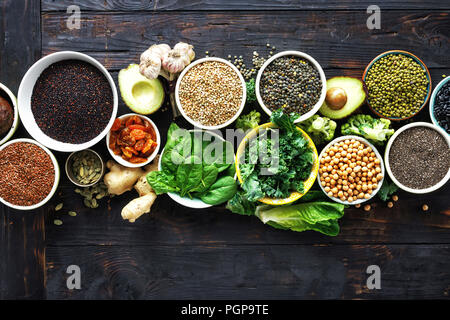 Vegetariano o dieta concetto alimentare. Impostare materie semi, cereali, fagioli, superfoods e verdura verde scuro su sfondo di legno vista superiore Foto Stock