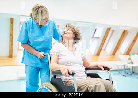 Cura il caregiver si prende cura di un senior donna in una sedia a rotelle a rehab Foto Stock