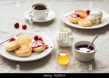 Tavolo per la colazione con frittelle di cagliata o pancake, caffè, marmellata e miele. Russo, Ucraino cucina. Colazione intima o comfort food concept Foto Stock