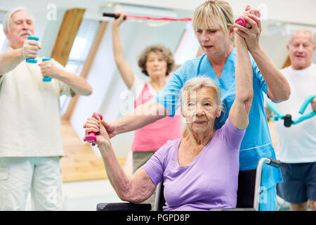 Vecchia donna treni con manubri in rehab classe e ottiene aiuto Foto Stock