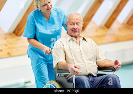 Senior uomo dopo la corsa in carrozzella è curato da assistente infermieristico cura Foto Stock