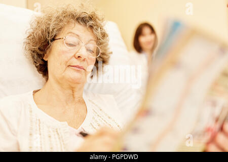 Senior donna leggendo un giornale nel letto di casa o in una casa di riposo Foto Stock