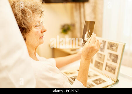 Senior donna guarda una foto dall'album di foto per il morbo di Alzheimer e demenza Foto Stock