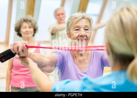 Senior donna nella classe di fisioterapia con trainer di fare esercizio con la fascia elastica Foto Stock