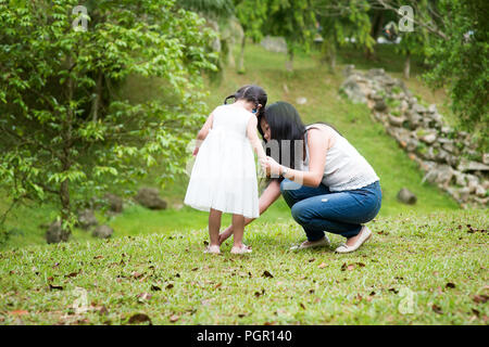 Madre contribuisce bambina indossa scarpa al parco. Famiglia asiatica all'aperto verticale. Foto Stock