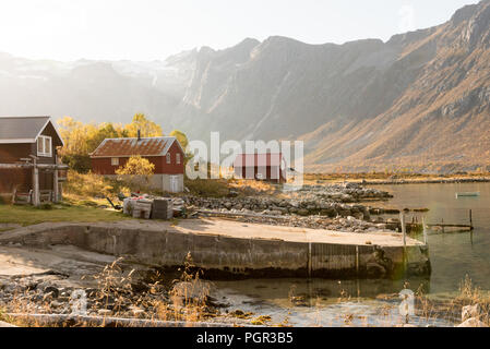 Fasci di luce con lens flare su un picco di montagna shining giù sopra una capanna sulla spiaggia in Tromso, Norvegia in una nebbiosa giornata in una scenografica landsc rurale Foto Stock