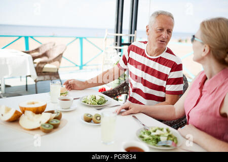 Età giovane seduto al tavolo serviti, con colazione e parlando a summer resort outdoor cafe Foto Stock