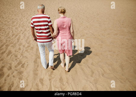 Affettuosa coppia senior in informale passeggiando per le spiaggia di sabbia sul caldo giorno d'estate Foto Stock