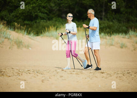 Uomo maturo e la donna in activewear parlando mentre passeggiate sulla spiaggia di sabbia Foto Stock