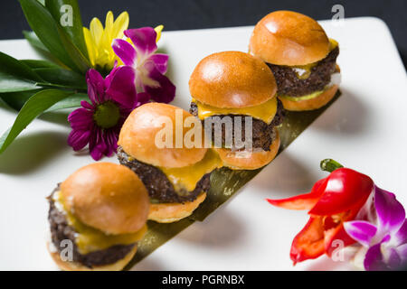 Fila di quattro formaggio hamburger cursori sulla piastra bianca con orchid Foto Stock