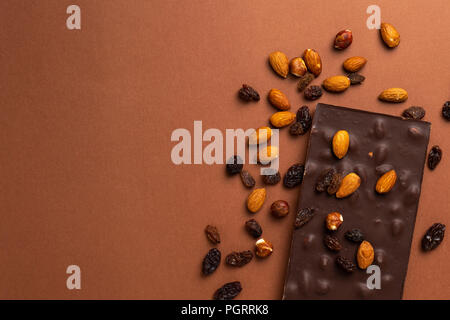 Dark chocolate bar con mandorle tostate e uvetta sparse su sfondo marrone Foto Stock