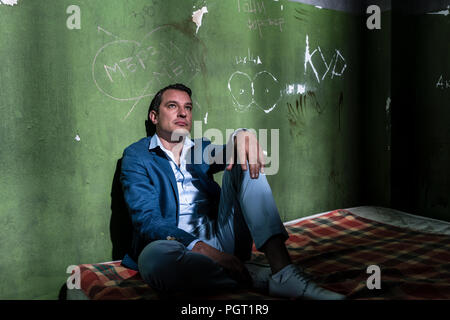 Premuto giovane uomo seduto su un materasso in una buia cella di prigione Foto Stock