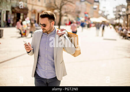 Ritratto di Allegro uomo bello va shopping in città mentre si utilizza il telefono cellulare Foto Stock