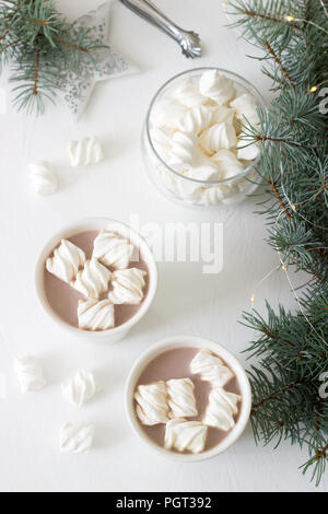 Il cacao con marshmelow in bianco tazze e marshmallows in un vasetto di vetro su un tavolo bianco con rami di abete rosso, una ghirlanda di fiori e una stella bianca. Messa a fuoco selettiva Foto Stock