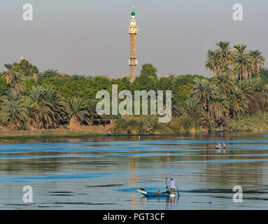 Egiziano uomo locale nella vecchia barca a remi la pesca con rete di mattina presto la luce del sole, con alto minareto della moschea, Fiume Nilo, Egitto, Africa Foto Stock