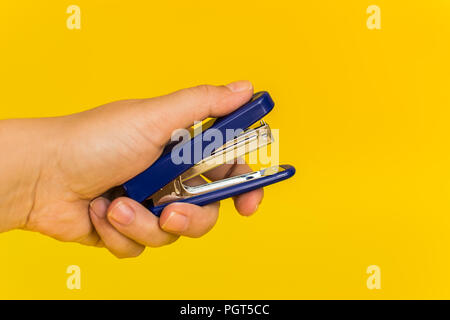 Mano che regge un ufficio blu cucitrice su uno sfondo giallo Foto Stock