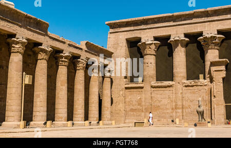 Guardia egiziana in uniforme bianca a piedi in corte di offerte cortile con colonne palmiformi, Tempio di Edfu, Egitto, Africa Foto Stock