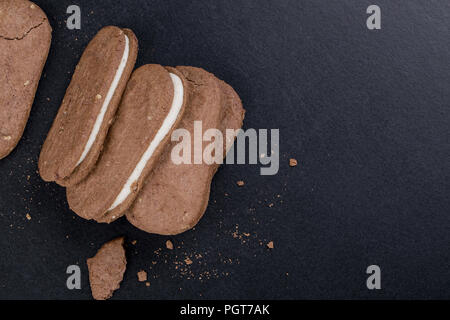 Sandwich di cioccolato i biscotti con la crema bianca ripieno su uno sfondo nero, close-up vista laterale Foto Stock