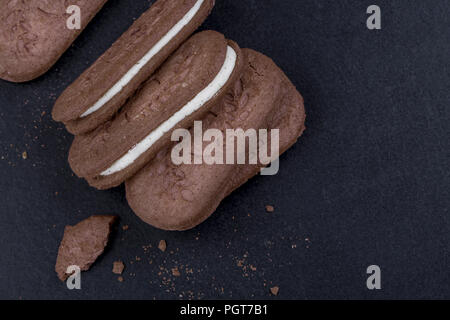 Sandwich di cioccolato i biscotti con la crema bianca ripieno su uno sfondo nero, close-up vista laterale Foto Stock