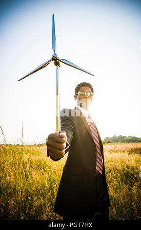 Un americano africano uomo tenendo un piccolo modello di turbina eolica. Concetto di energia verde / green business Foto Stock
