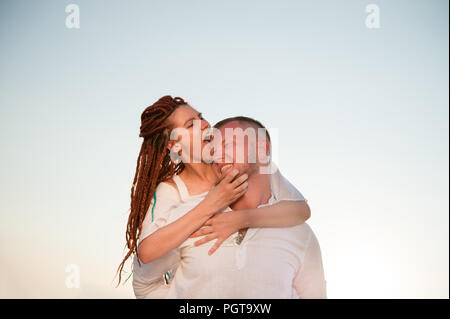 Funny graziosa ragazza caucasica con dreadlocks di mordere il suo grazioso boyfrieng seduto sul suo retro Foto Stock