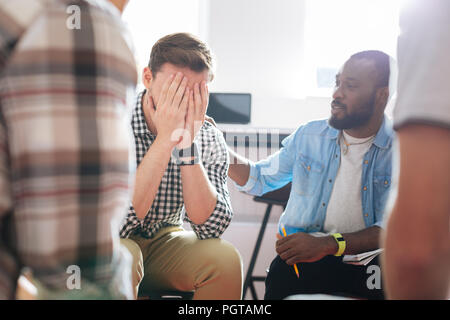 Uomo infelice nasconde la sua faccia e piangere mentre è in sessione psicologico Foto Stock