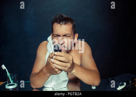 Il giovane uomo in camera da letto seduto di fronte allo specchio di graffiare la sua barba a casa. Le emozioni umane concept Foto Stock