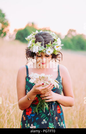 La ragazza con la corona di fiori che pongono nel campo durante il tramonto Foto Stock