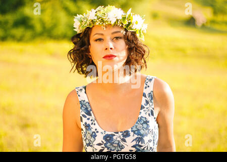 La ragazza con la corona di fiori che pongono nel campo durante il tramonto Foto Stock