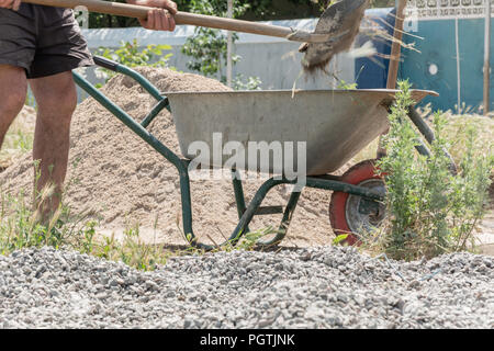 Lavoratore usare la pala e riempire la carriola con rifiuti di costruzione. Strumenti di costruzione. Lavoratore con la pala e il carrello su ruote sulla costruzione di t Foto Stock