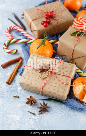 I mandarini freschi con foglie, candy canes, confezioni regalo in carta kraft e spezie - cannella, anice e chiodi di garofano su uno sfondo blu Foto Stock