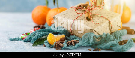 I mandarini freschi con foglie, candy canes, confezioni regalo in carta kraft e spezie - cannella, anice e chiodi di garofano su uno sfondo blu Foto Stock