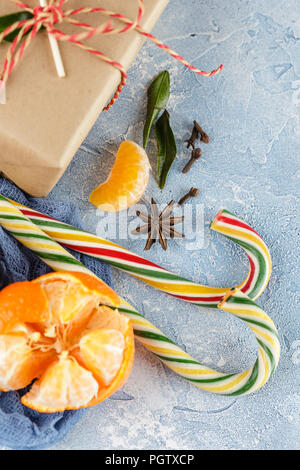 I mandarini freschi con foglie, candy canes, confezioni regalo in carta kraft e spezie - cannella, anice e chiodi di garofano su uno sfondo blu Foto Stock