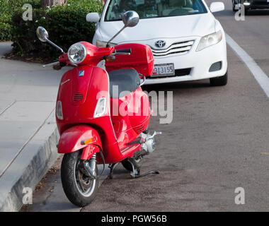 Un rosso scooter Vespa parcheggiata di fronte un bianco auto sulla strada in Encinitas, CALIFORNIA, STATI UNITI D'AMERICA Foto Stock