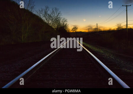 Mercurio, Venere e Luna crescente linea il cielo della sera sopra il sole di setting ed un set di binari ferroviari. Foto Stock