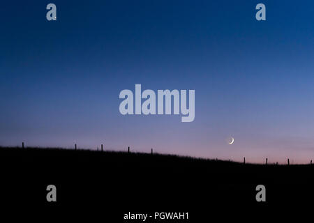 Lo skyline culle mezzaluna nel bagliore pallido del pastello twilight al di sotto di Venere, un vecchio recinto è visibile lungo le dolci colline. Foto Stock