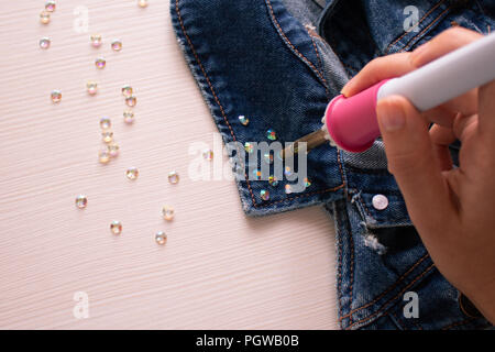 Decorazione a mano. Un processo di saldatura strass sul colletto di una camicia di denim da saldatore Foto Stock