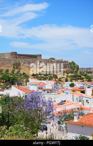 Vista in elevazione del castello e la città di edifici con una graziosa struttura Jacaranda in piena fioritura in primo piano, Castro Marim, Algarve, Portogallo, dell'Europa. Foto Stock