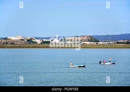 Vista sul Fiume Guadiana verso la città bianca e il suo forte e castello con i pescatori in piccole imbarcazioni in primo piano, Castro Marim, Algarve, Foto Stock