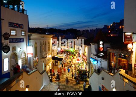 Vista in elevazione del R 5 de Outubro, la strada dello shopping di sera con turisti che si godono la impostazione, Albufeira, Portogallo, Europa. Foto Stock