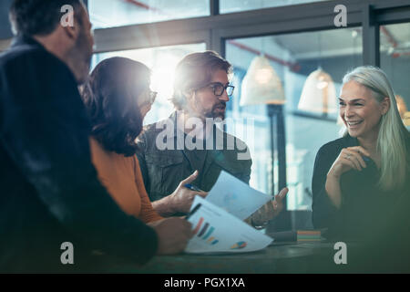 Sorridente coppia business donna parlando con i colleghi durante la riunione. Un gruppo di persone in piedi intorno a un tavolo e discutere di lavoro. Foto Stock