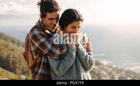 Ritratto di giovane e bella coppia in vacanza. L'uomo abbracciando la sua ragazza da dietro, sia in piedi su una scogliera. Foto Stock